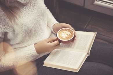 Photo of Woman with cup of coffee reading book at home, closeup