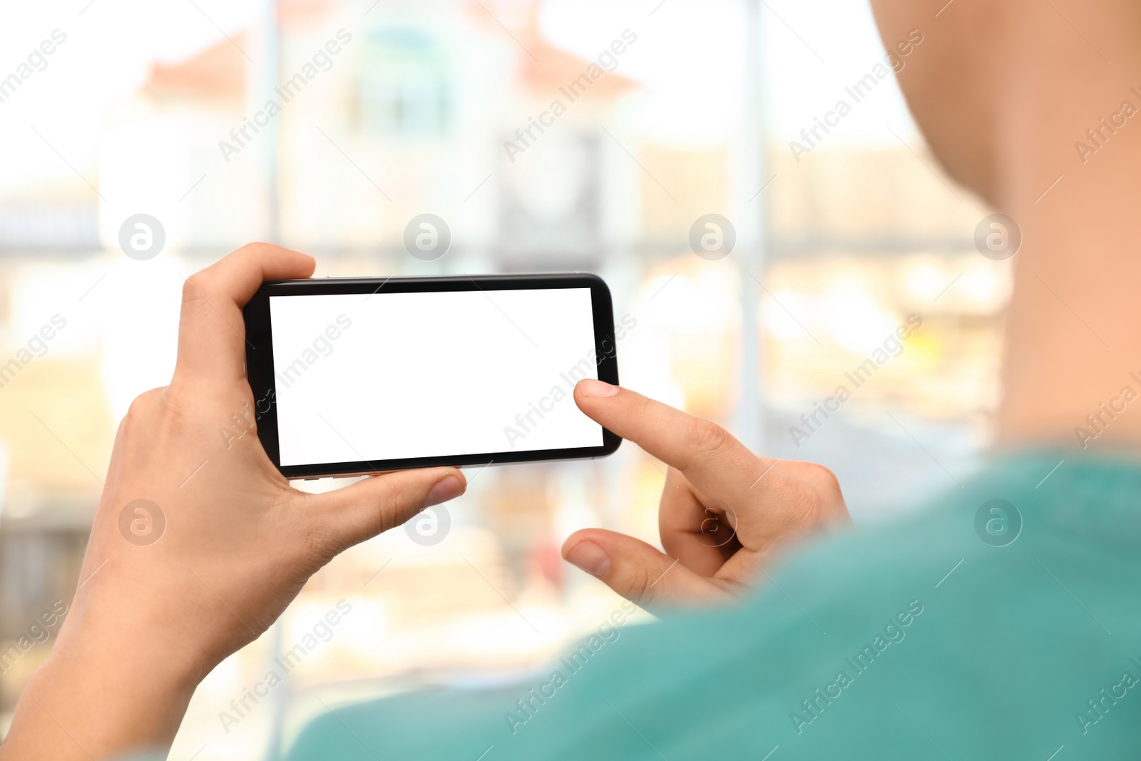 Photo of Man holding smartphone with blank screen on blurred background, closeup of hands. Space for text