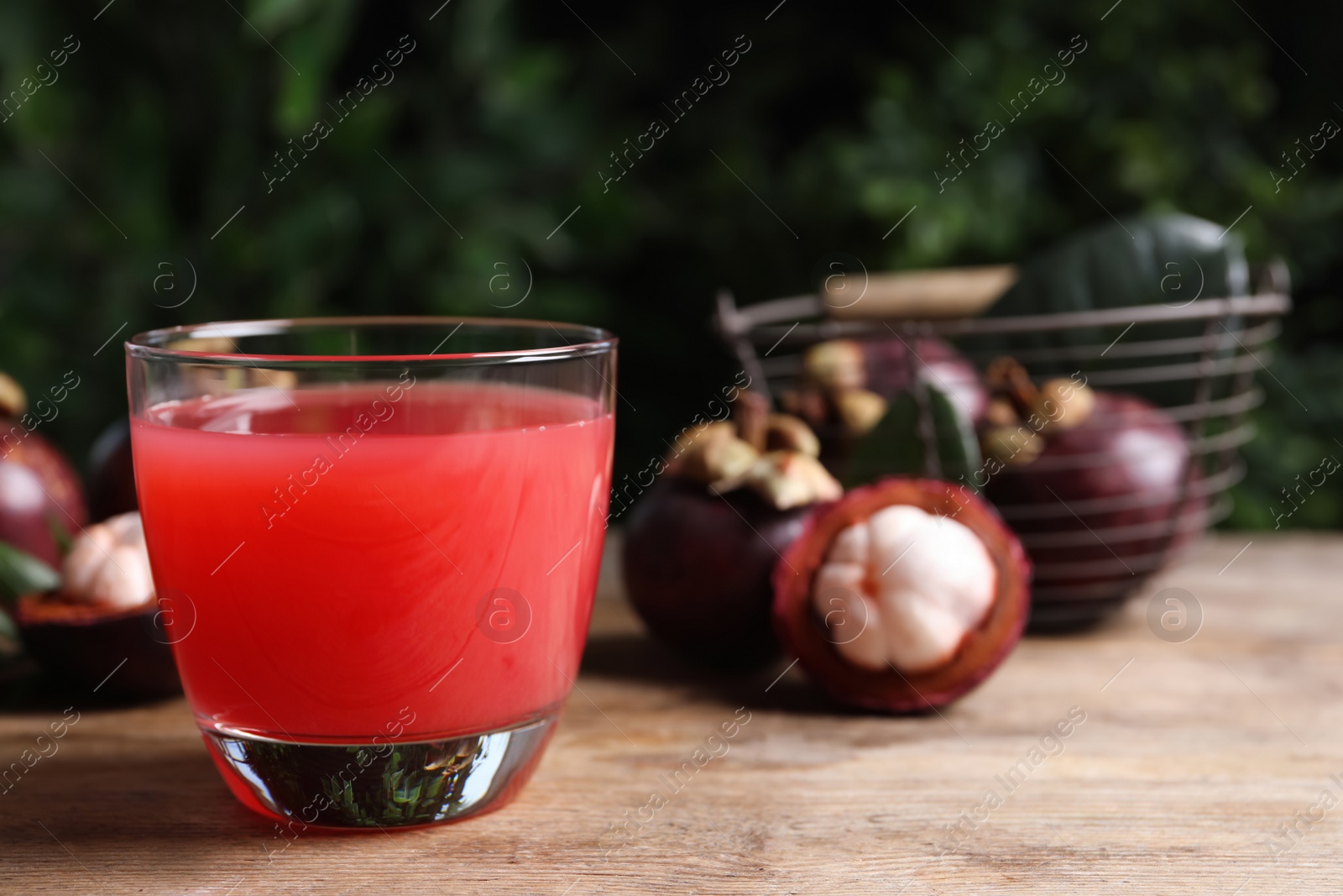 Photo of Delicious mangosteen juice in glass on wooden table, space for text