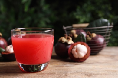 Delicious mangosteen juice in glass on wooden table, space for text