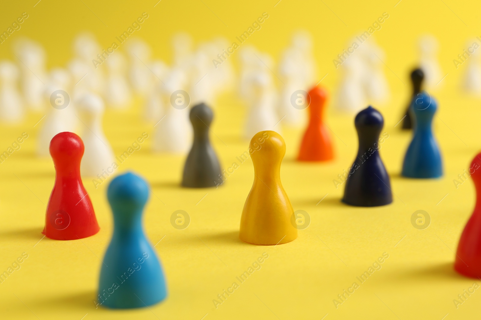 Photo of Colorful pawns on yellow background, closeup. Social inclusion concept