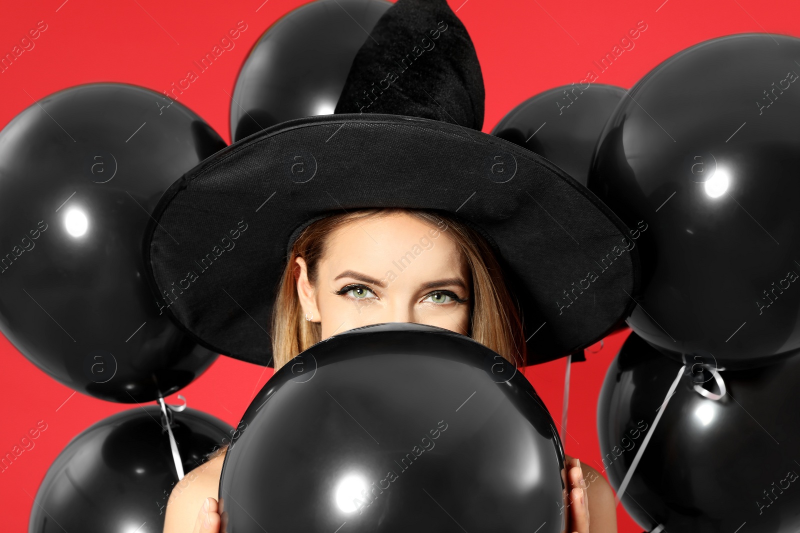 Photo of Beautiful woman wearing witch costume with balloons for Halloween party on red background