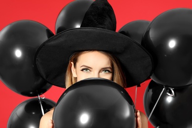 Beautiful woman wearing witch costume with balloons for Halloween party on red background