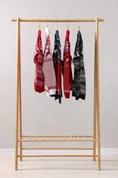 Different Christmas sweaters hanging on rack against light background