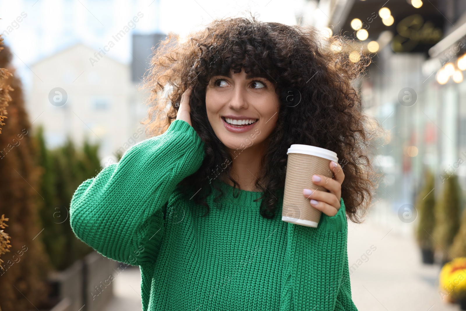 Photo of Happy young woman in stylish green sweater with cup of coffee outdoors