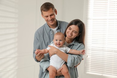 Photo of Happy family. Couple with their cute baby near window indoors