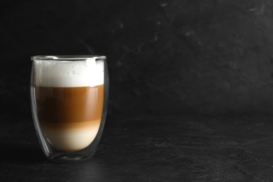 Photo of Hot coffee with milk in glass on black table. Space for text