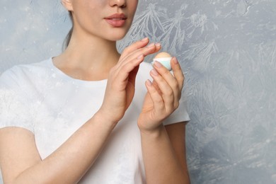 Winter skin care. Closeup of woman applying lip balm on grey background, frost effect. Space for text
