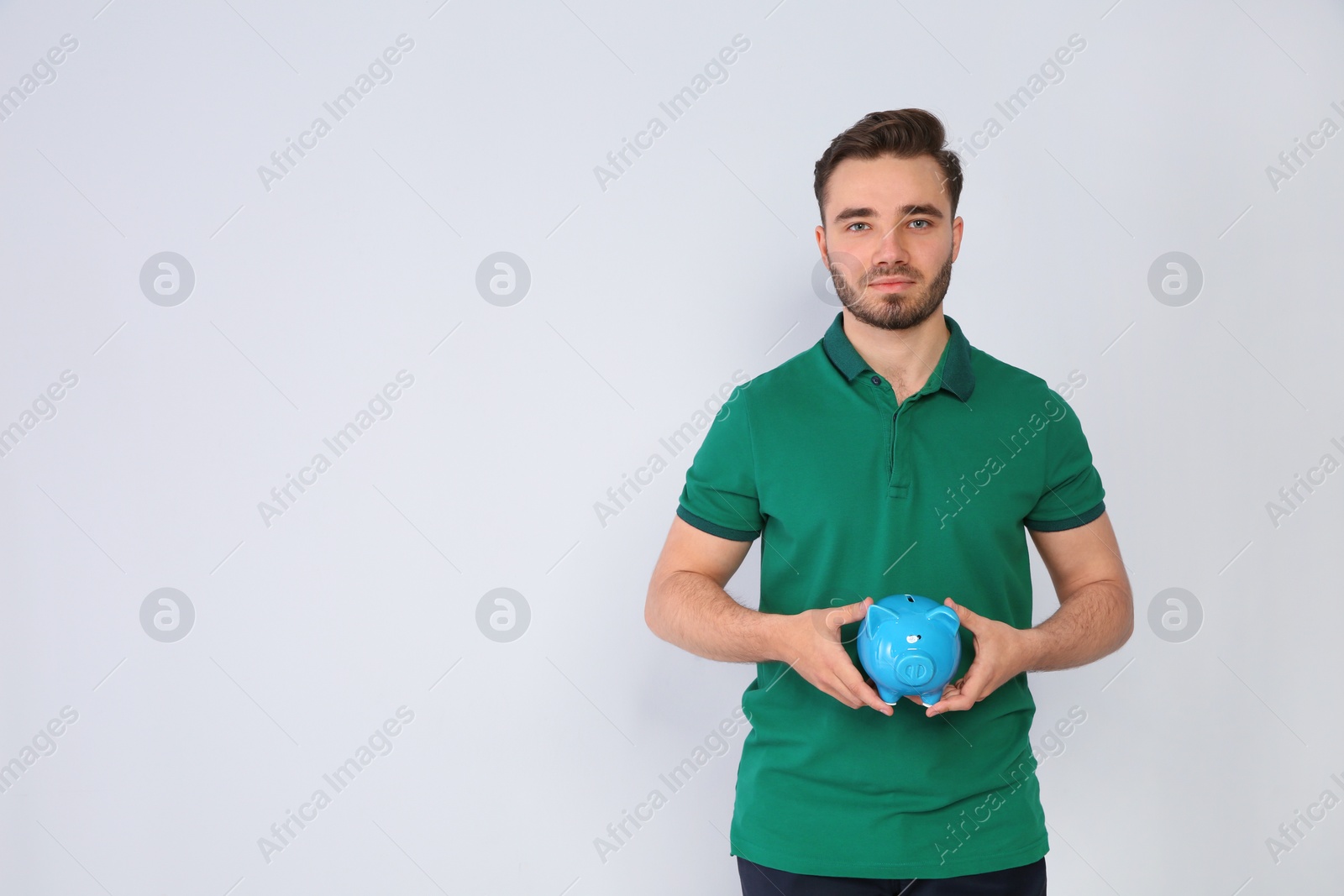 Photo of Young man with piggy bank on light background. Space for text