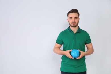 Young man with piggy bank on light background. Space for text