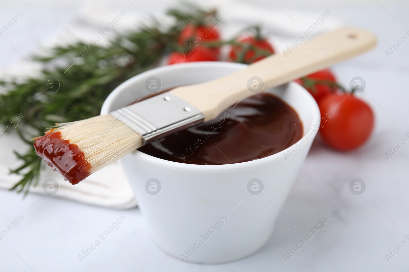 Photo of Marinade in bowl and basting brush on white table, closeup