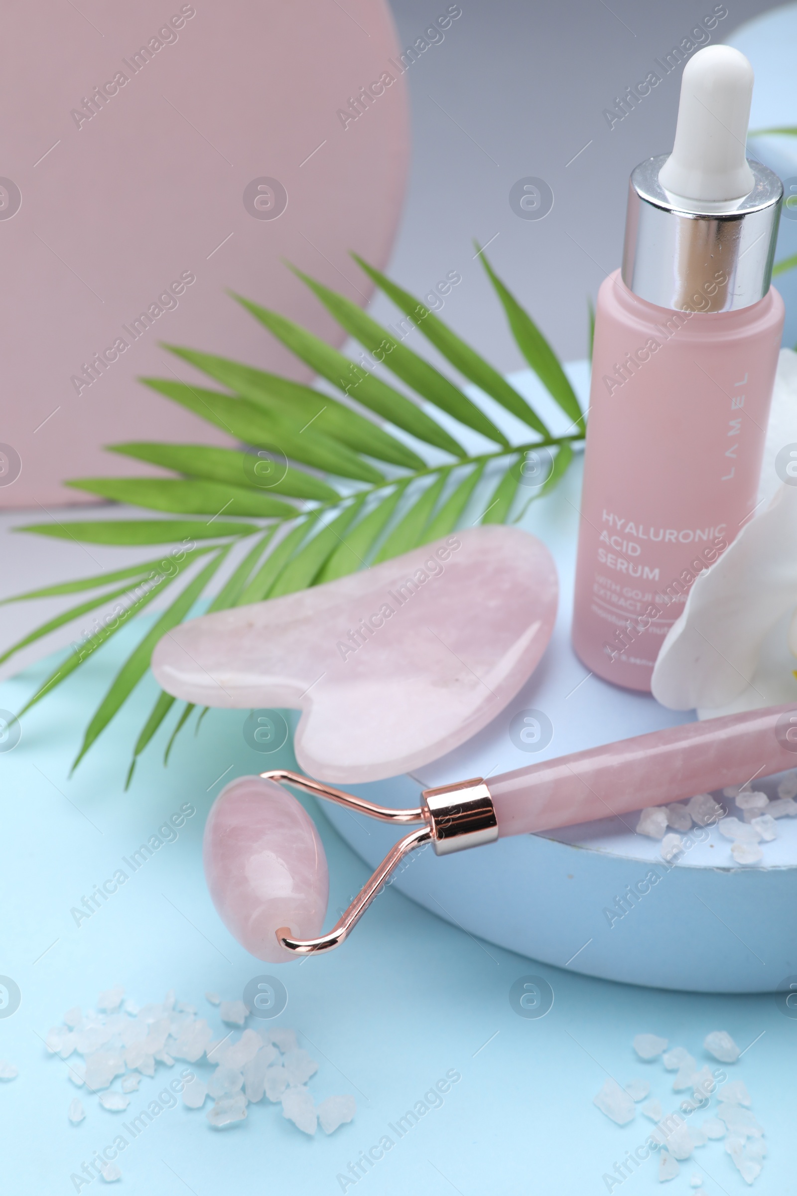 Photo of Beautiful composition with gua sha stone, face roller and bottle of serum on color background