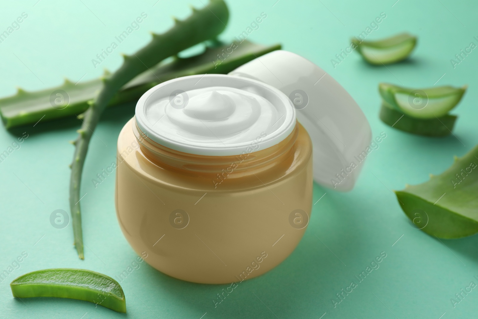 Photo of Jar of natural cream and aloe leaves on green background, closeup