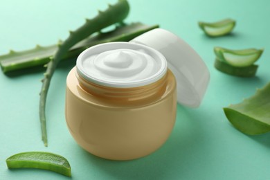 Photo of Jar of natural cream and aloe leaves on green background, closeup