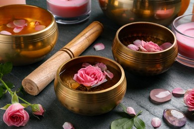 Photo of Tibetan singing bowls with water, beautiful rose flowers and mallet on gray table, closeup