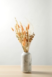Photo of Dried flowers in vase on table against light background