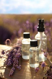 Photo of Bottles of lavender essential oil on wooden table in field