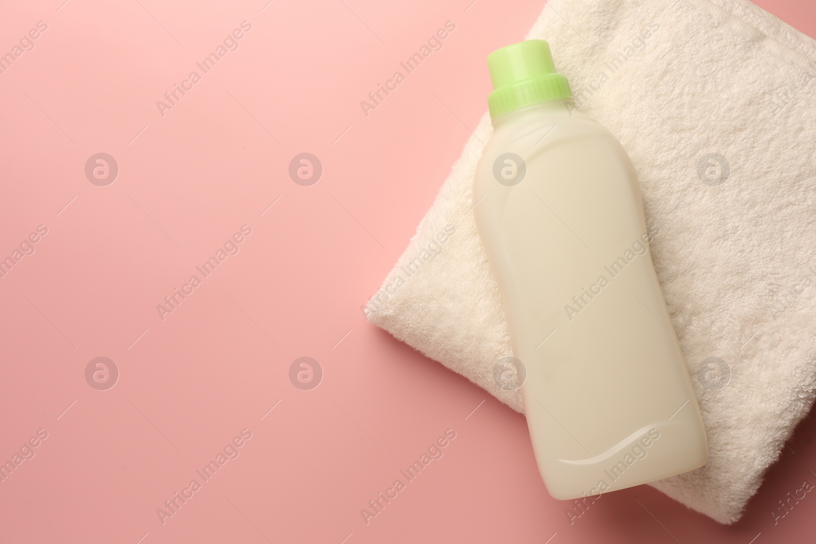 Bottle of fabric softener and terry towel on pink background, top view. Space for text Photo of Bottle of fabric softener and terry towel on pink background, top view. Space for text