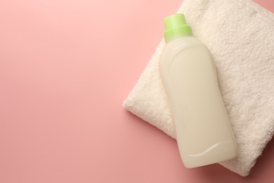 Photo of Bottle of fabric softener and terry towel on pink background, top view. Space for text