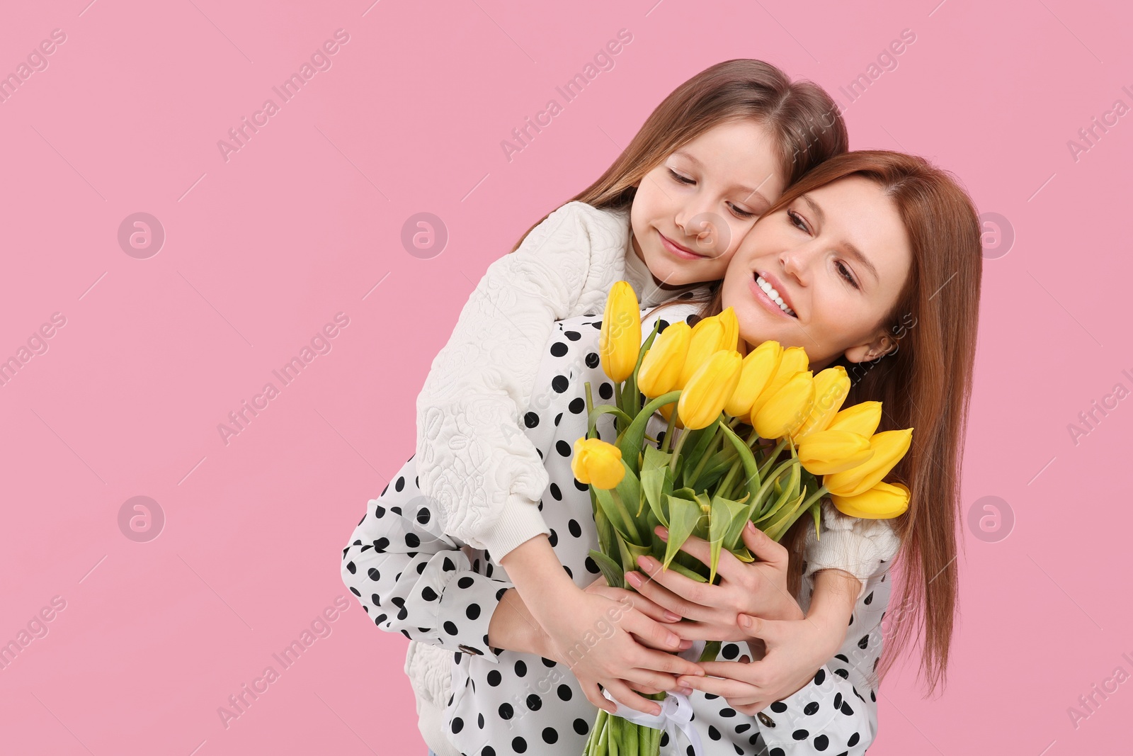 Photo of Mother and her cute daughter with bouquet of yellow tulips on pink background. Space for text