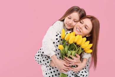 Mother and her cute daughter with bouquet of yellow tulips on pink background. Space for text