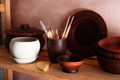 Set of different crafting tools and clay dishes on wooden rack in workshop