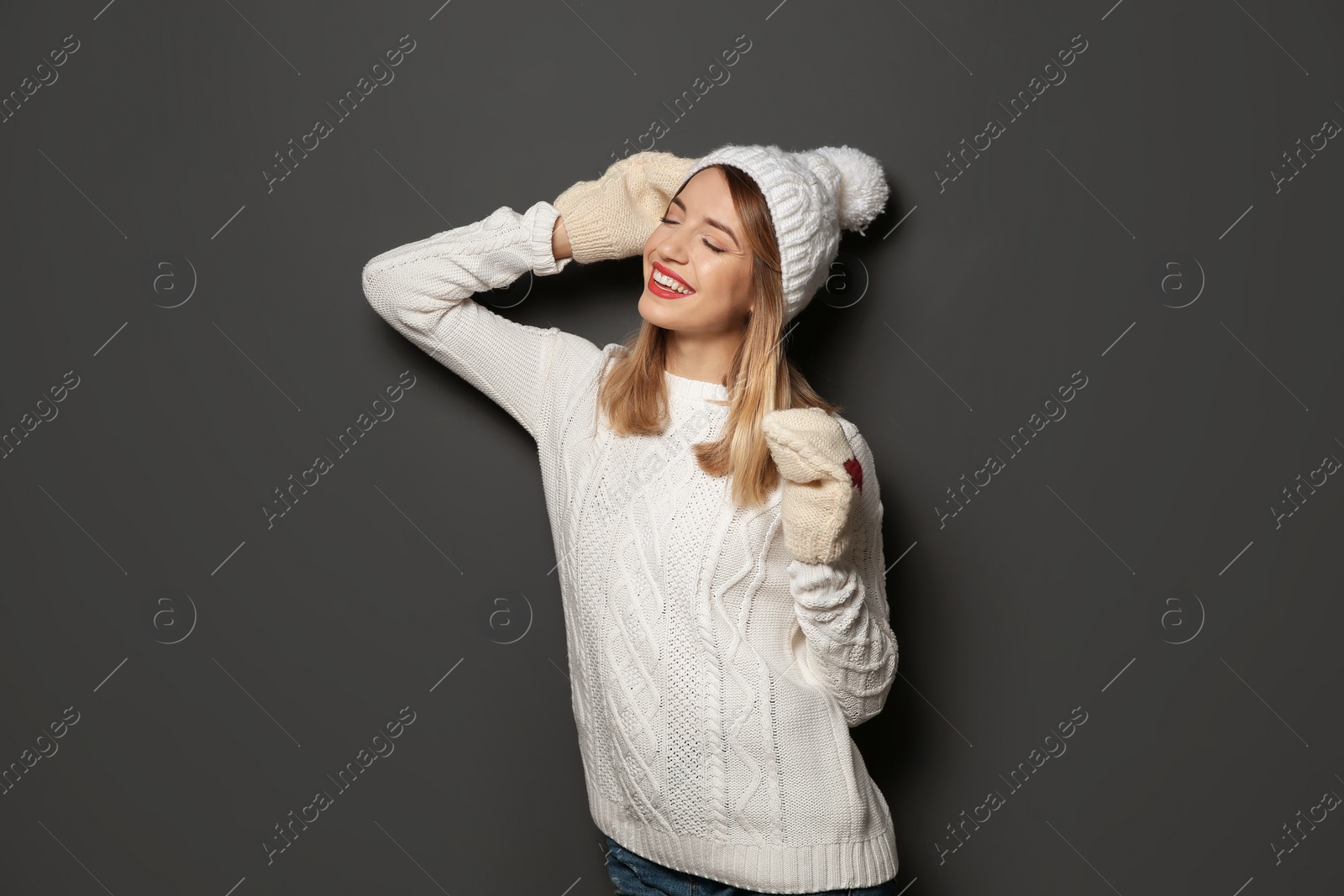Photo of Beautiful young woman in warm sweater with hat and mittens on dark background