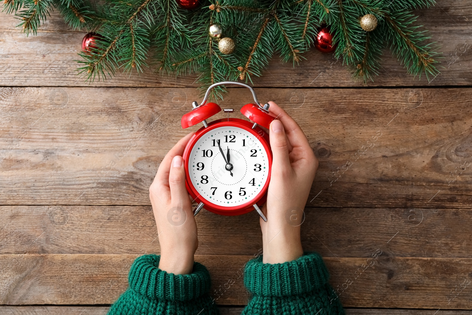 Photo of Woman holding alarm clock near Christmas decor over wooden background, top view. New Year countdown