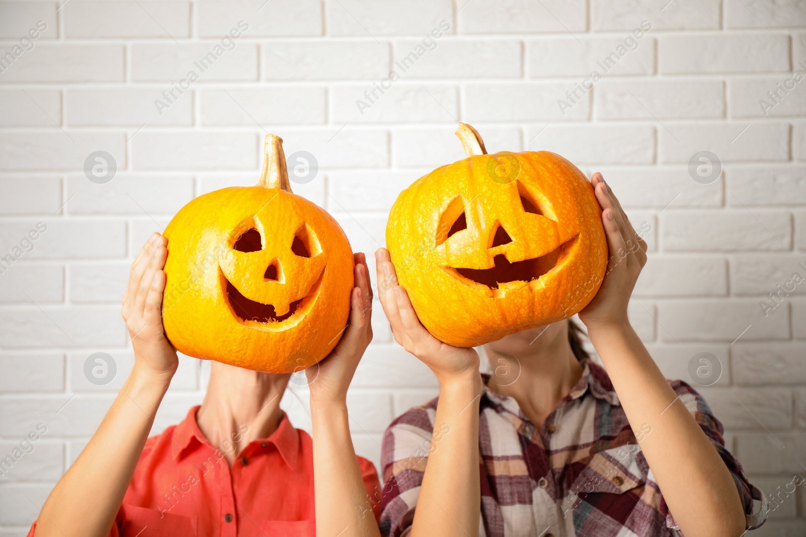 Photo of Women with pumpkin heads near white brick wall. Jack lantern - traditional Halloween decor