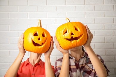 Photo of Women with pumpkin heads near white brick wall. Jack lantern - traditional Halloween decor