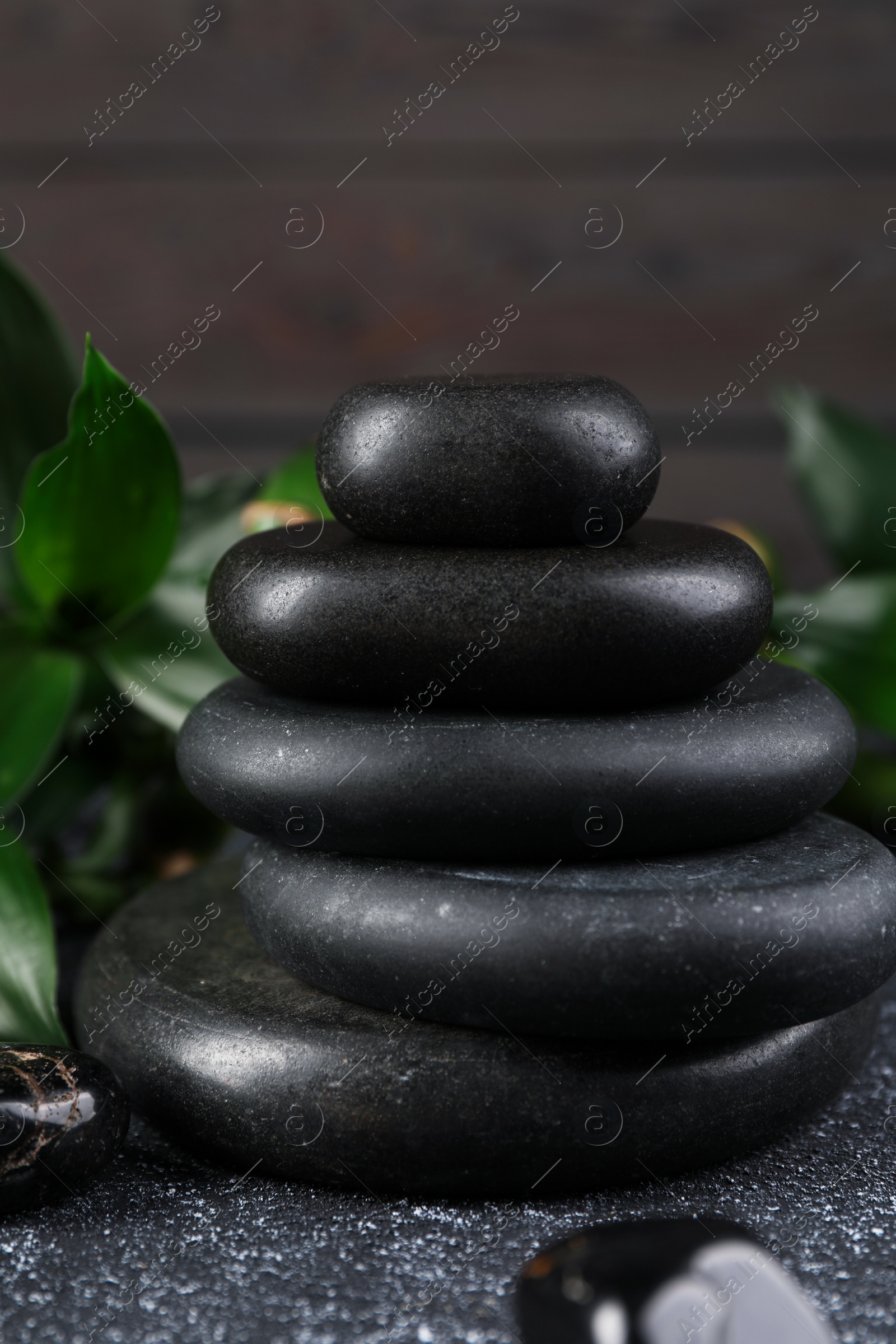 Photo of Stacked spa stones and bamboo leaves on black textured table, closeup