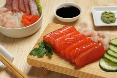 Delicious sashimi set of salmon and shrimps served with cucumbers, parsley, wasabi and soy sauce on wooden table, closeup
