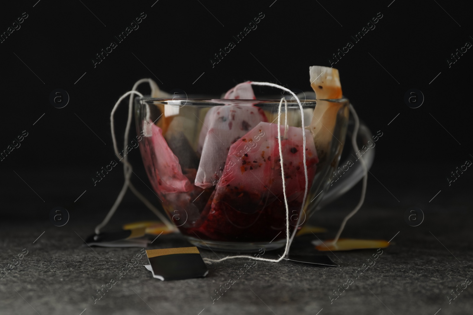 Photo of Many used tea bags in glass cup on grey table