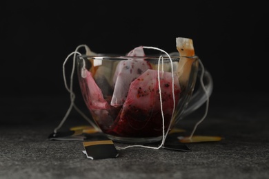 Photo of Many used tea bags in glass cup on grey table