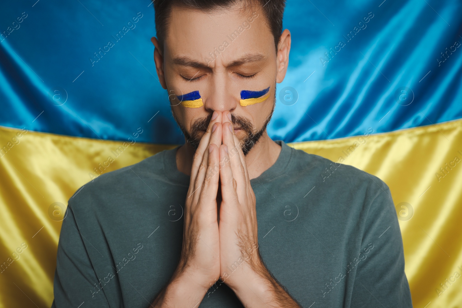 Photo of Man with clasped hands praying near Ukrainian flag, closeup