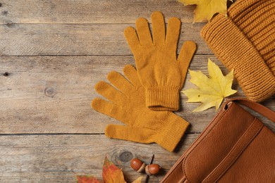 Flat lay composition with stylish orange woolen gloves and dry leaves on wooden table. Space for text