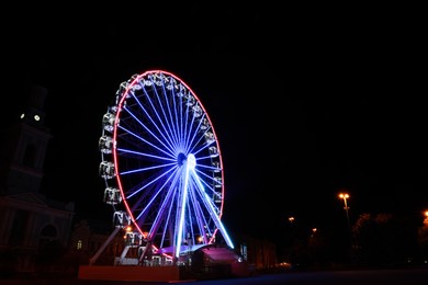 Photo of Beautiful glowing Ferris wheel on city street at night. Space for text
