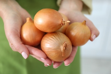 Photo of Woman holding golden onions on blurred background, closeup