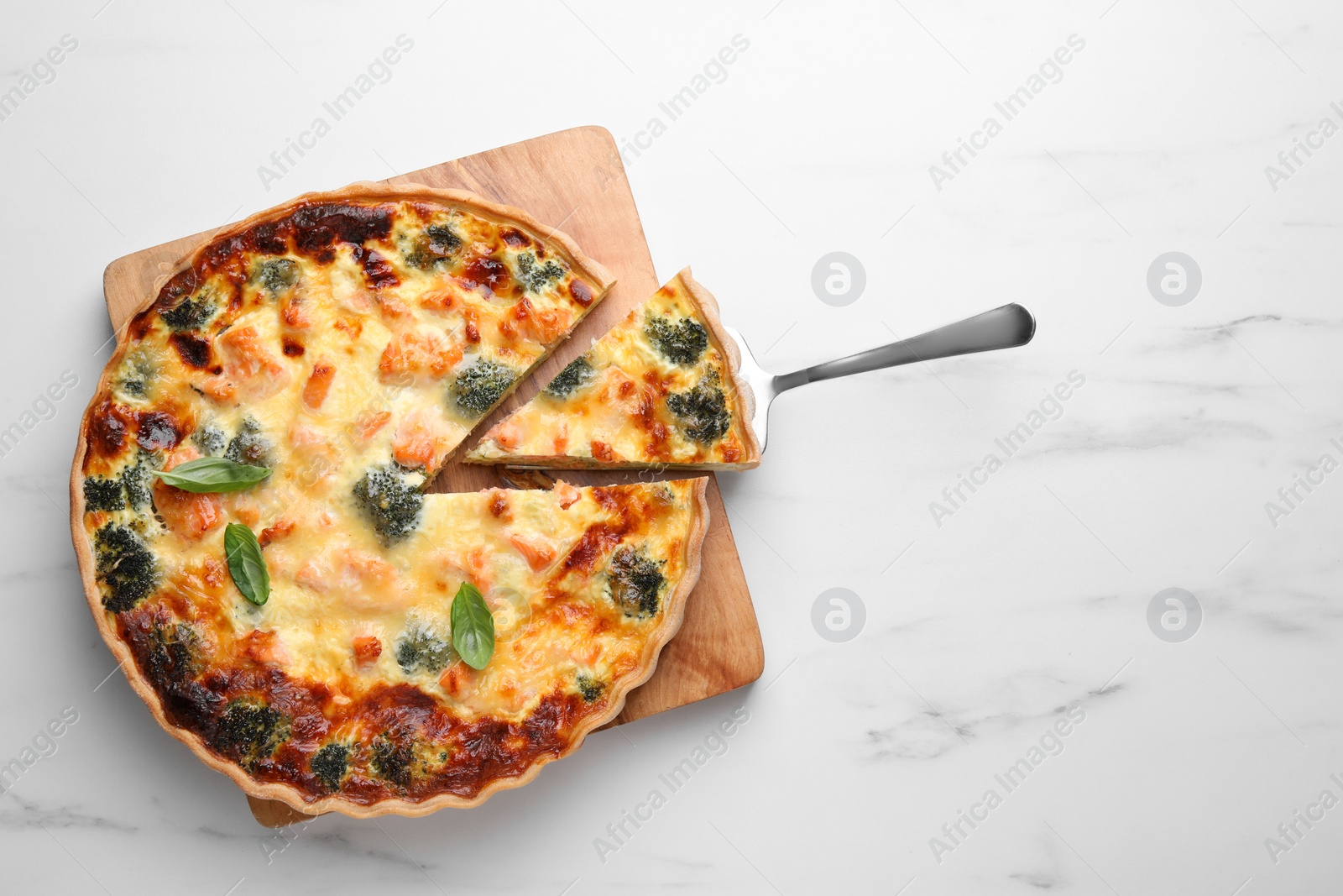 Photo of Delicious homemade salmon quiche with broccoli and spatula on white marble table, top view. Space for text