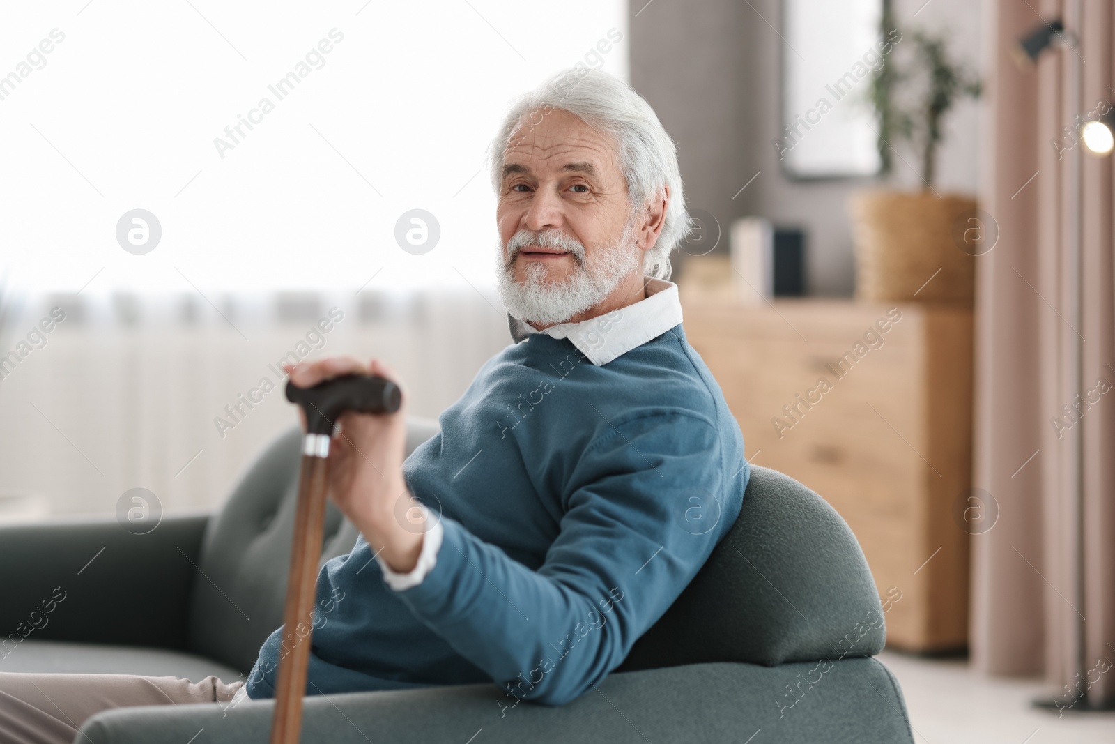 Photo of Portrait of happy grandpa with walking cane sitting on sofa indoors