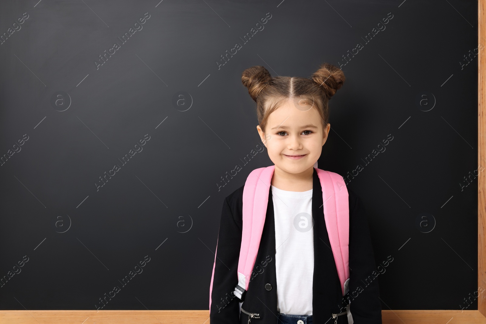 Photo of Happy little school child with backpack near chalkboard. Space for text