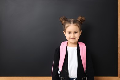 Happy little school child with backpack near chalkboard. Space for text