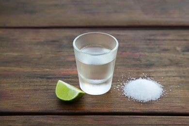 Photo of Mexican tequila shot with lime slice and salt on wooden table. Drink made from agave