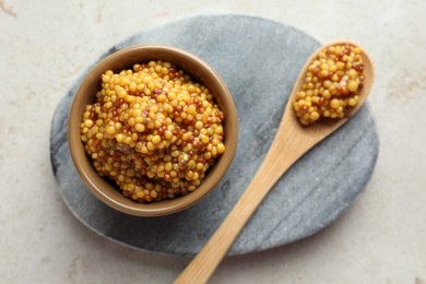 Bowl and spoon with whole grain mustard on light table, top view