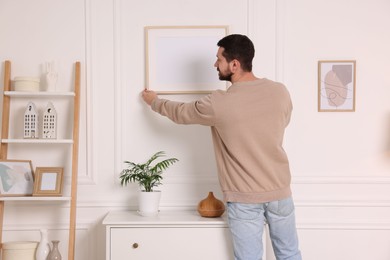 Photo of Man hanging picture frame on white wall at home