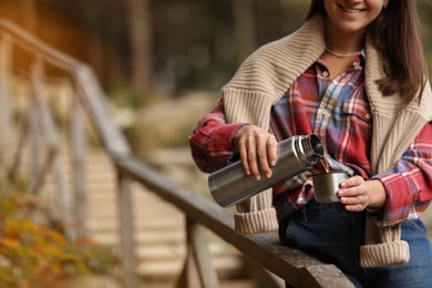 Woman pouring hot drink from metallic thermos into cup lid outdoors, closeup. Space for text