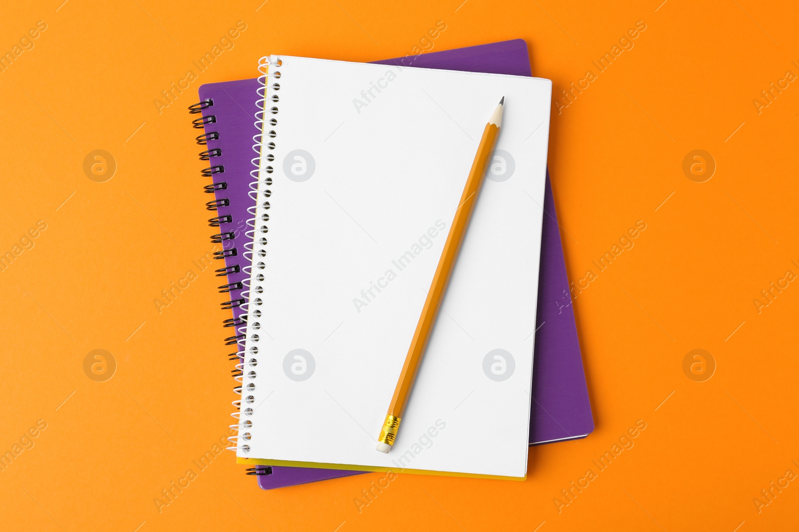 Photo of Notebooks with pencil on orange background, top view