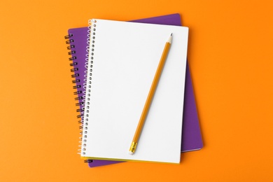 Photo of Notebooks with pencil on orange background, top view