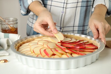 Photo of Woman putting apple slices into baking dish with dough to make traditional English pie at white table, closeup