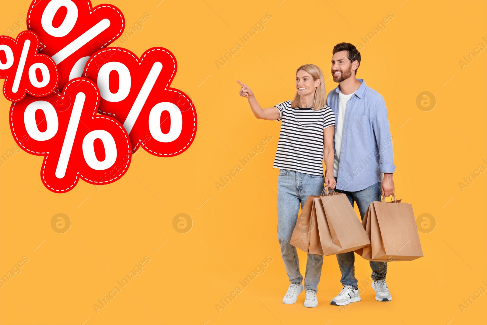 Image of Discount offer. Happy couple with paper shopping bags looking at illustrations of percent signs on orange background